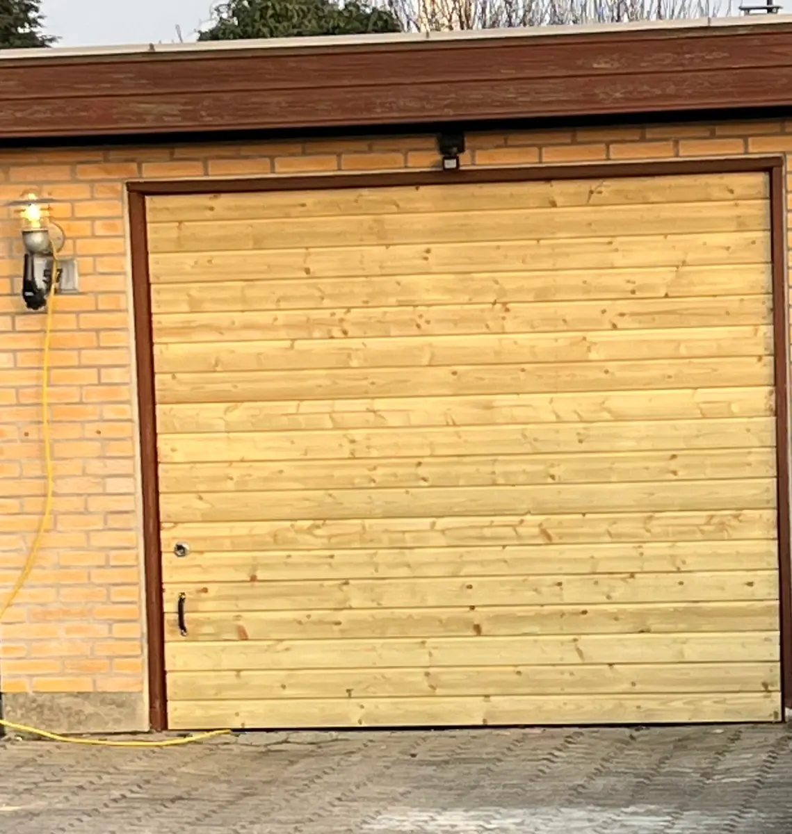 Garageport beklædt med nye vandrette brædder i lyst træ, sat i mellem gulstensvæg og brun trærammefacade