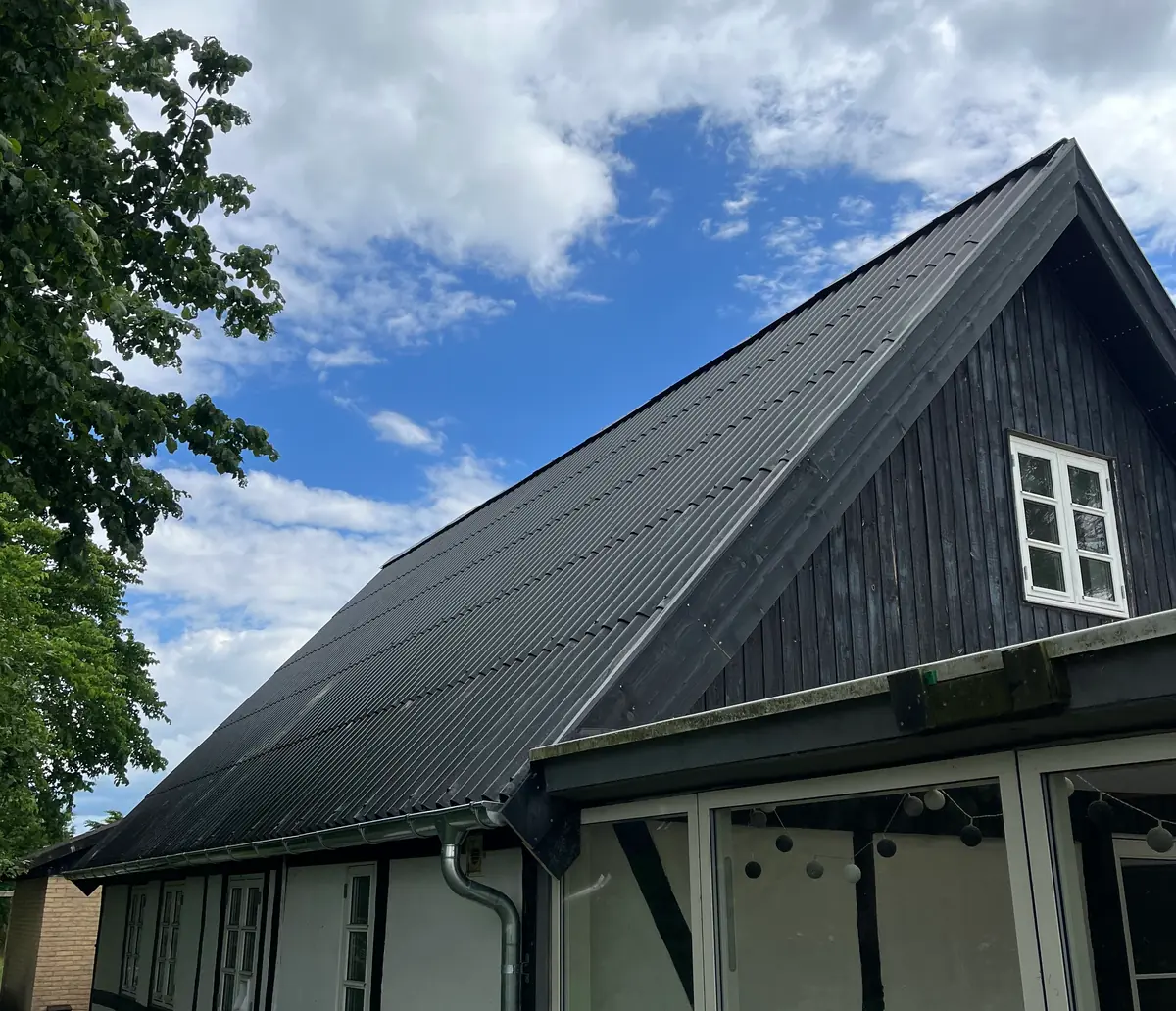 Hel tagflade lagt færdig med nye mørke bølgeplader, ført helt ud til en sortmalet bræddegavl med hvidt sprossevindue og zinktagrende